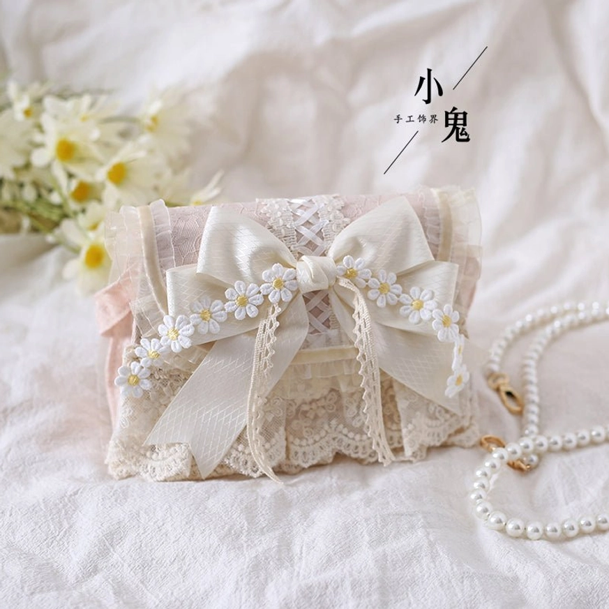 Pink and ivory lolita handbag with pearl chain strap detail, front left oblique view on white cloth with yellow daisy flowers