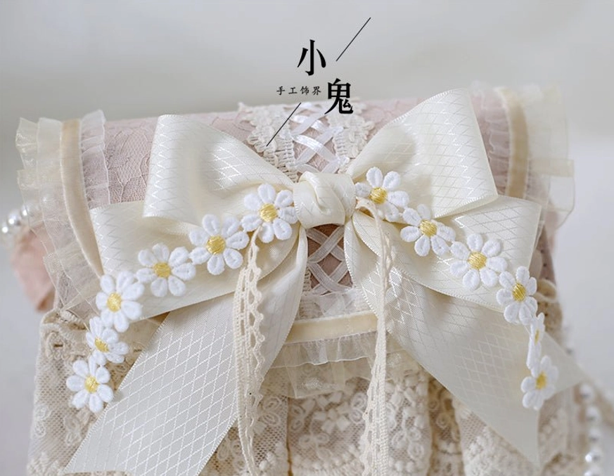 Close-up detail of ivory lace lolita handbag showing satin bow and tiny daisy embellishments, frontal detail view white surface