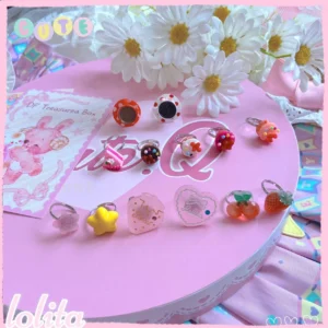 Complete kawaii lolita dessert ring collection featuring miniature cupcake heart star and strawberry designs in assorted pastel candy colors displayed on pink round table with white daisies