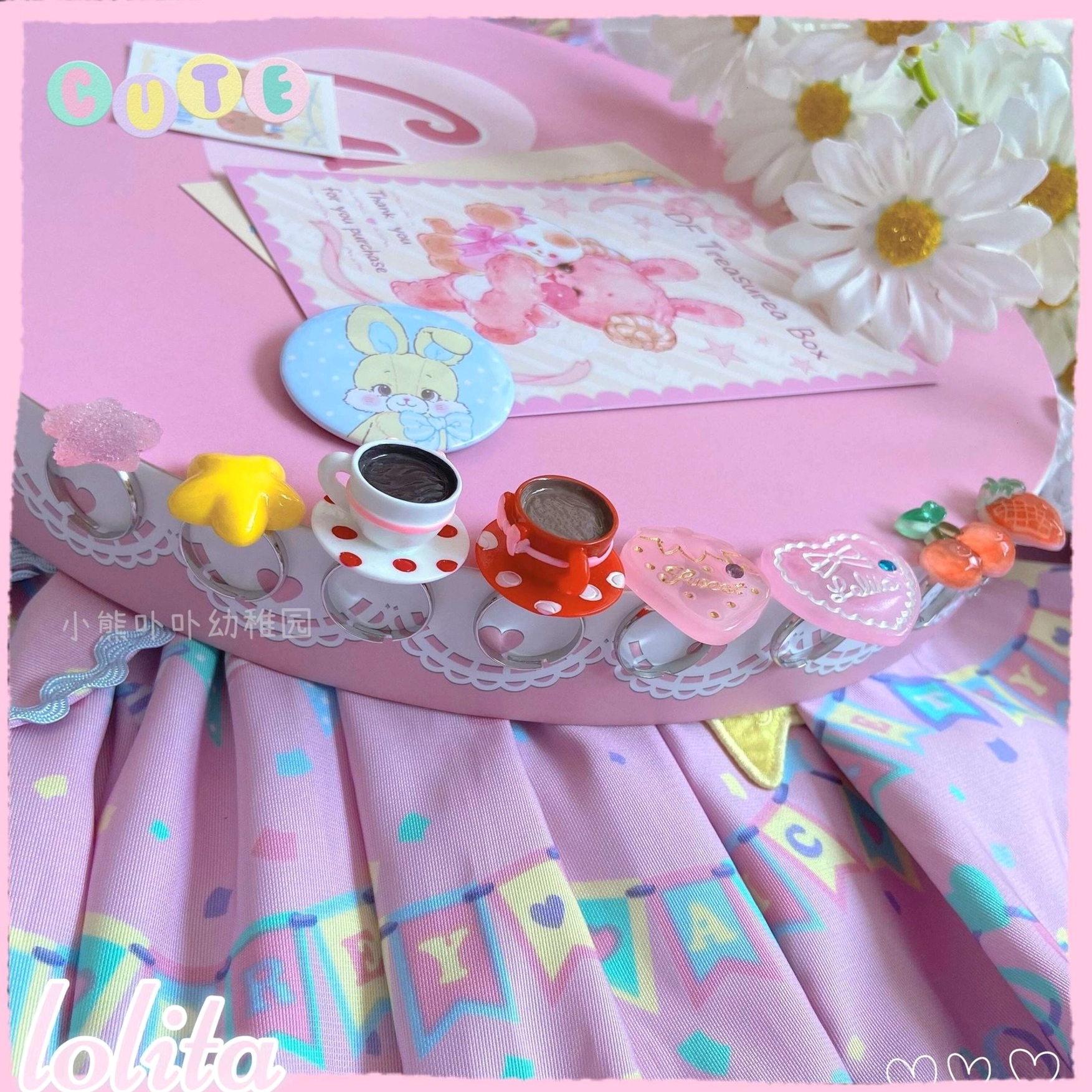 Loose kawaii lolita dessert ring collection with mixed bright and pastel candy colors displayed on pink table with white daisies and bunny postcards