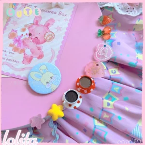 Assorted kawaii lolita dessert rings and enamel badge arranged on pink pastel lolita skirt fabric with geometric patterns and hearts