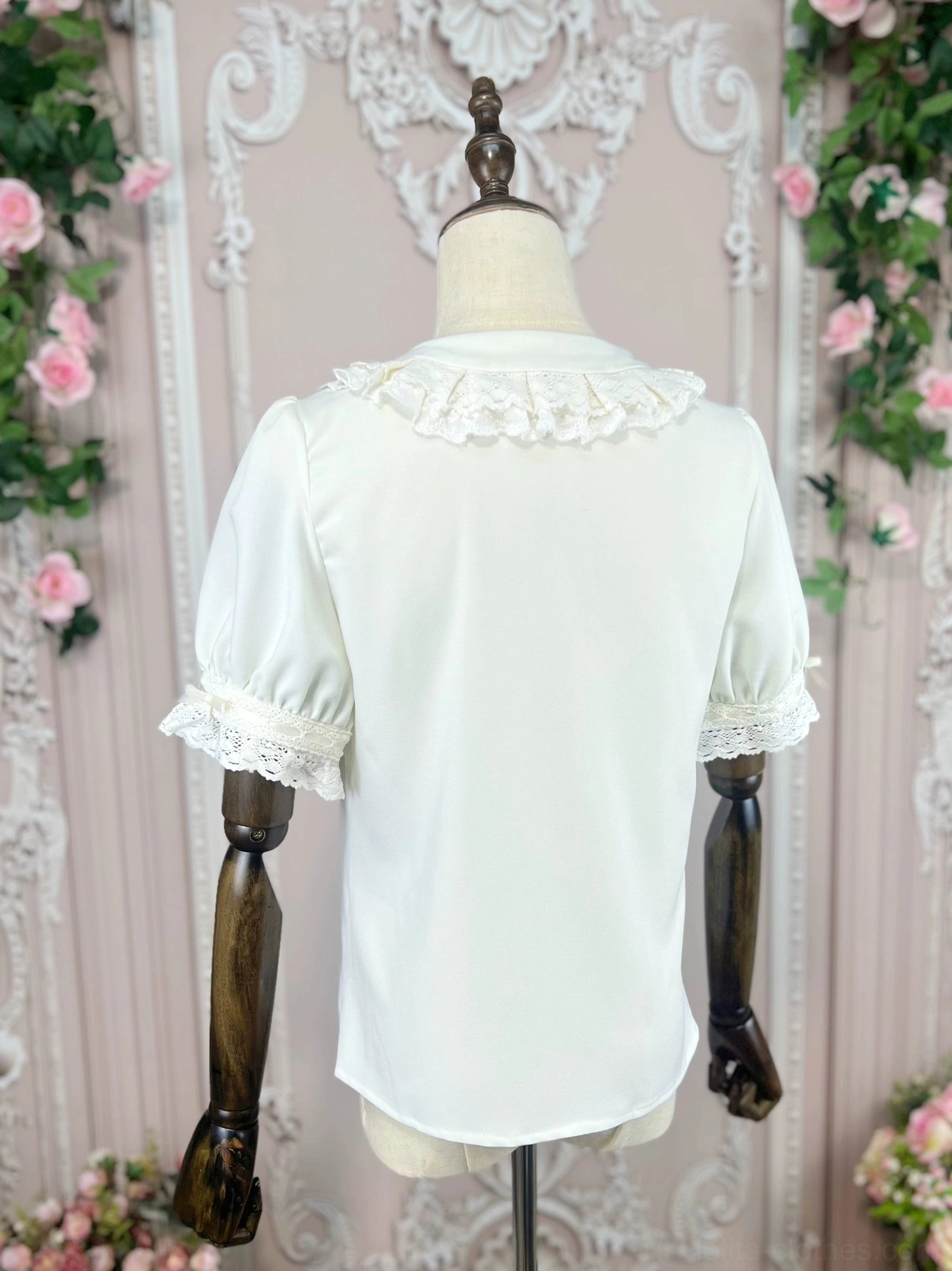 Lolita blouse rear view showing ruffled lace back collar plain back fabric and lace trimmed puff sleeves against simple vintage carved wall background