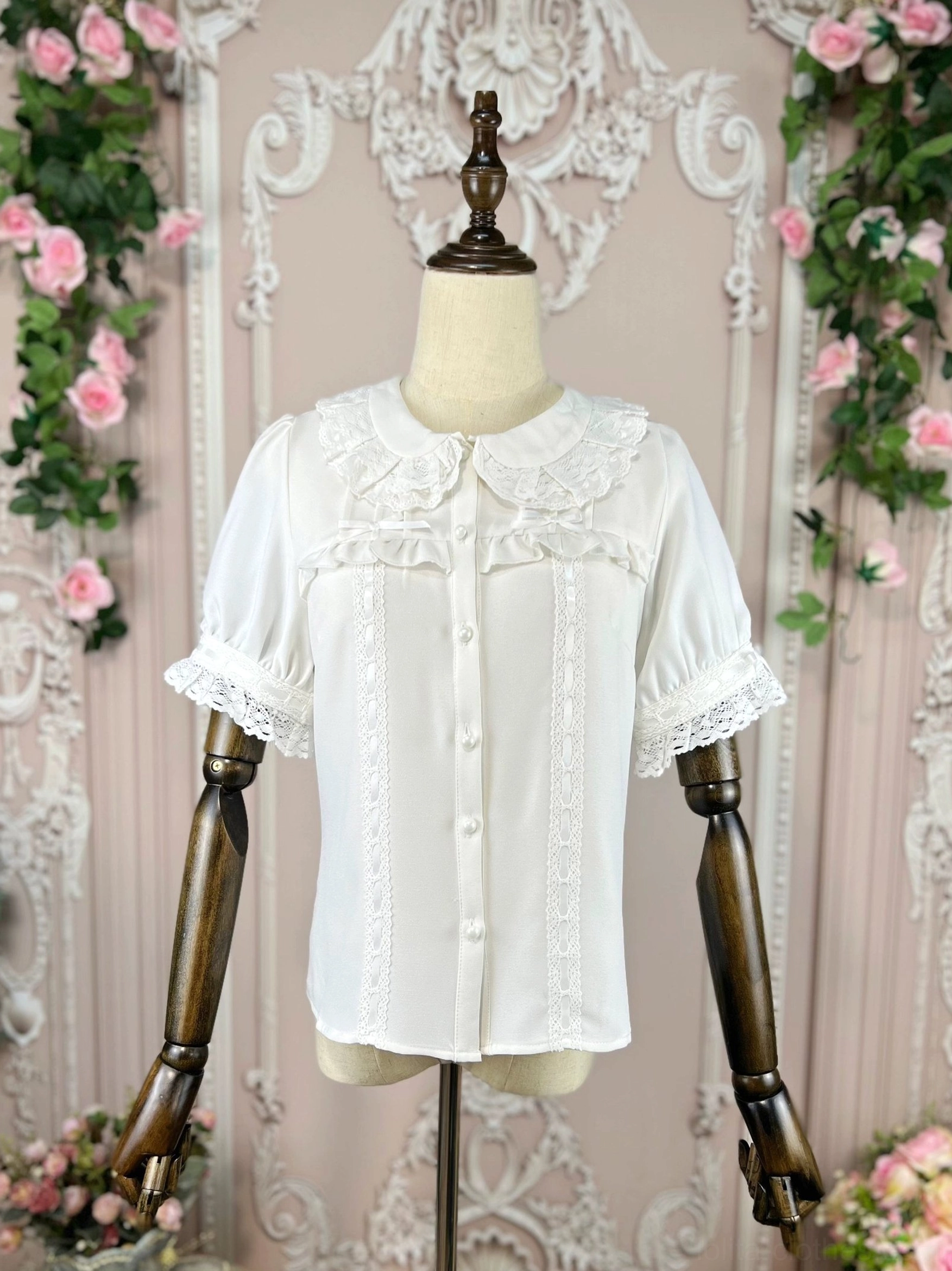 Lolita vintage doll collar blouse on mannequin in slight side front view clearly showing vertical lace trim on front placket against retro carved floral European backdrop