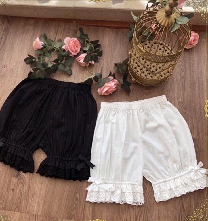 Overhead flat lay of elegant lolita elastic waist cotton bloomers featuring black and white variants with multi-layer ruffled embroidered lace hems, displayed on vintage wooden table with pink roses and decorative ornamental birdcage, showcasing premium cotton craftsmanship and color palette options