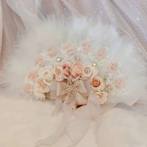 Handmade Lolita tea party feather fan with white fluffy feather base, bouquet of artificial pink roses, layered pearl flowers, satin ribbon bow and gem brooch, flat lay frontal view on plush fabric