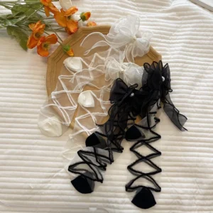Flat lay top-down view of lolita gauze ankle socks with pearl bows and cross stripes displayed on decorative tray with floral props, showing both black and white colorway options