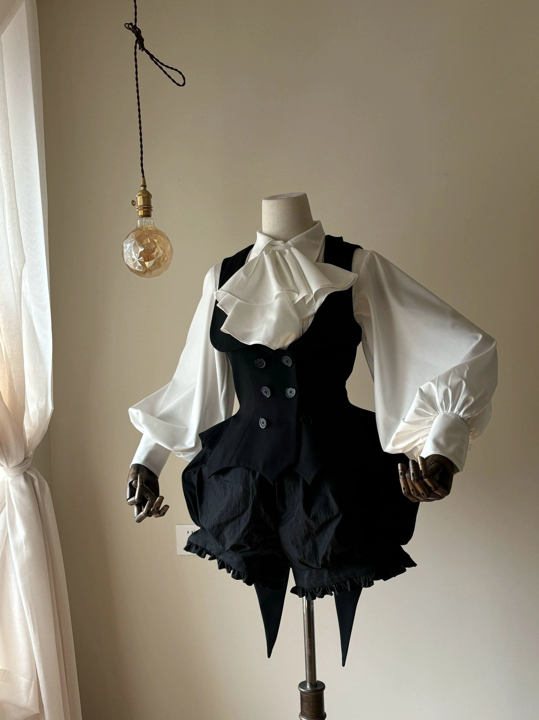 Gothic Lolita gentleman-style ensemble with white detachable ruffled neck cravat, puffed long-sleeve blouse, black waistcoat and ruffled bloomer shorts with bat tail, right three-quarter front angle
