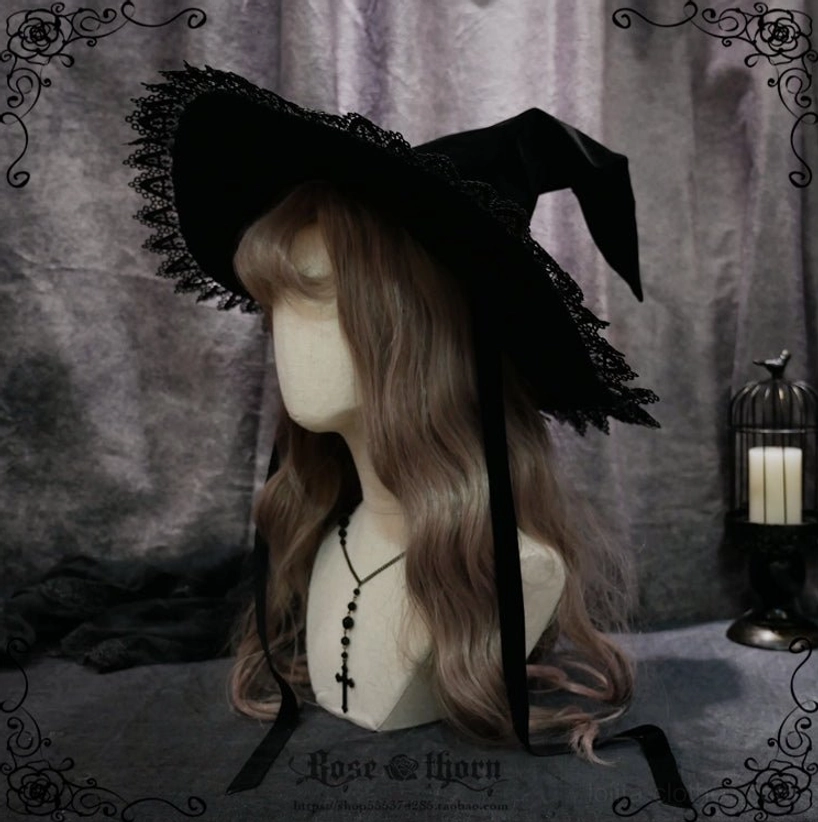 Pointed top lolita witch hat side view worn on mannequin with brown curly wig, displaying lace-trimmed brim and long black ribbon strap against dark retro background with candle lantern