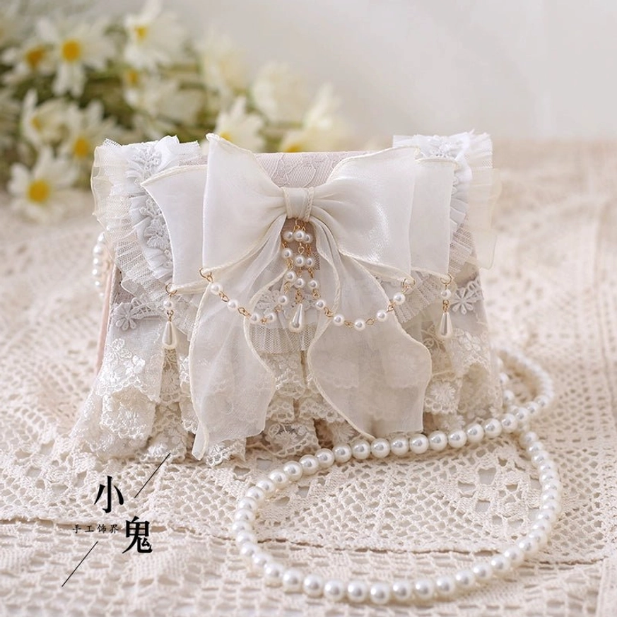 Close-up flat lay ivory lolita handbag showing decorative bow and pearl tassel ruffled lace edge with pearl chain