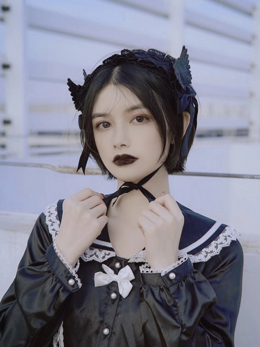 Half-body view girl in black sailor lolita outfit wearing wing-decorated black hairband with matching neck strap outdoor rooftop background