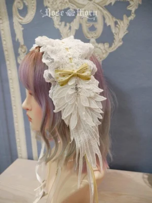 Lolita headdress angel wings design left profile view on mannequin, embroidered white wings with yellow satin bow, long trailing satin ribbons, tabletop display