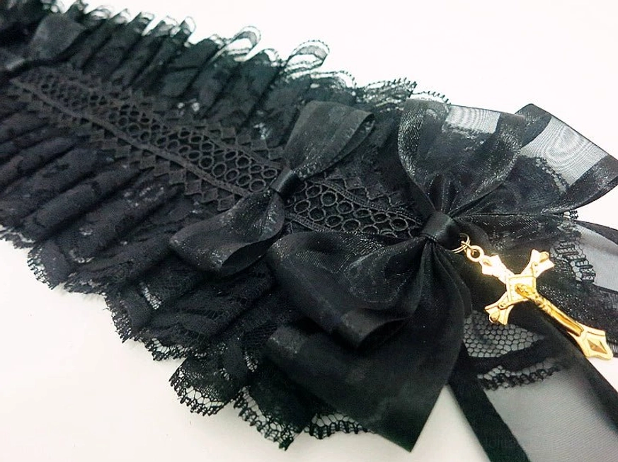 Flat lay close-up detail of gothic lolita headband featuring intricate black lace ruffles, satin bows, embroidered mesh fabric, and ornate gold cross charm on white background