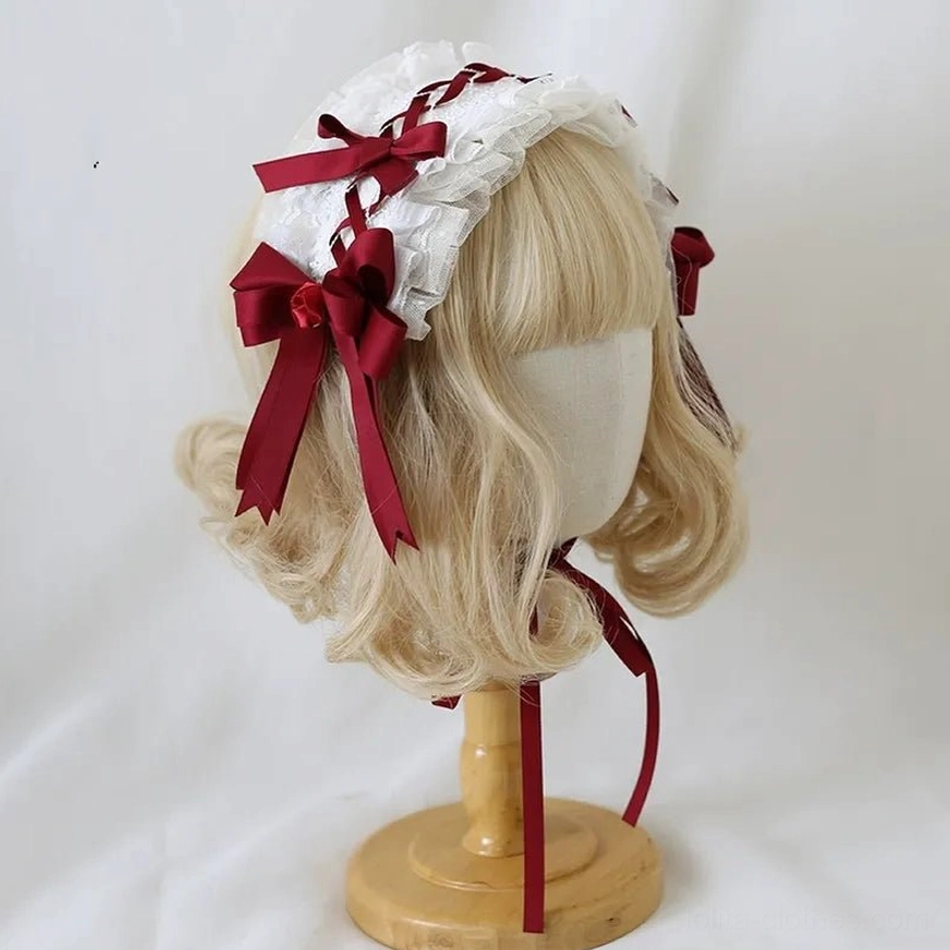 Dark red lolita headdress three-quarter side angle on wooden display mannequin head featuring white frilled lace with wine-red satin bows and long ribbon fixing strap