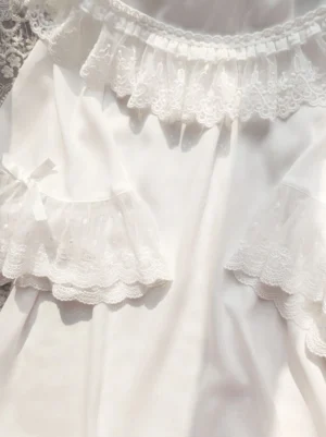 Close-up detail view of sweet lolita inner blouse showing double-layered lace ruffles at round neckline and flutter sleeve cuffs with delicate satin bows on lace fabric background