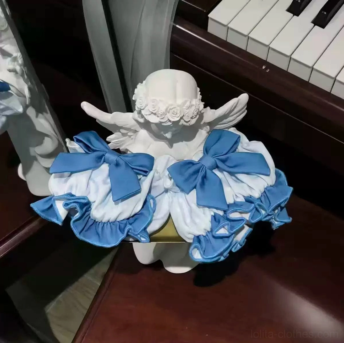 Lolita JSK back detail display top-down close-up view on piano surface showing dual oversized blue bows, tiered ruffled skirt layers, angel wing decoration prop, skirt volume and construction