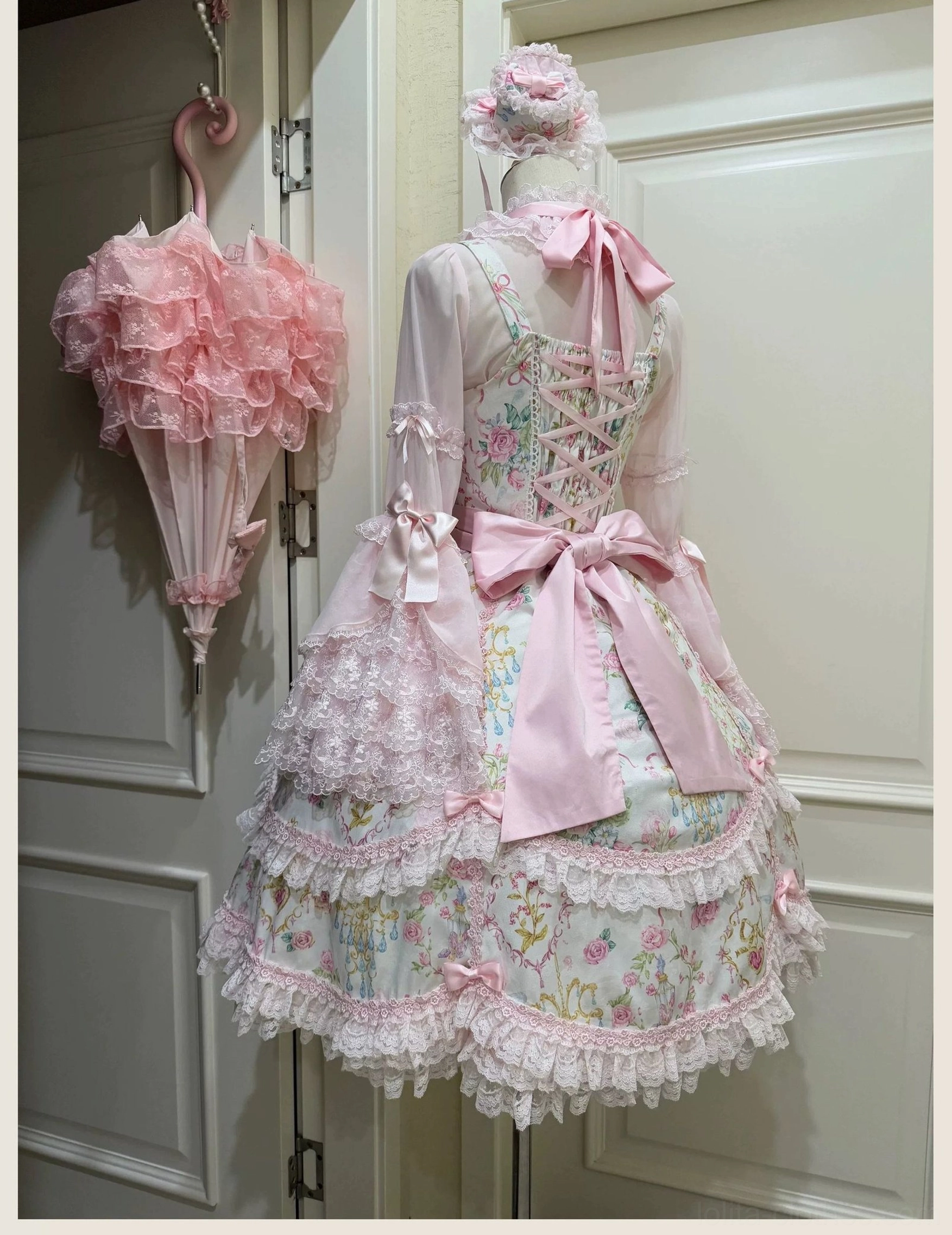 Old school Lolita JSK dress back view showing lace-up corset back, large satin bow, layered lace skirt trim and matching pink lace umbrella