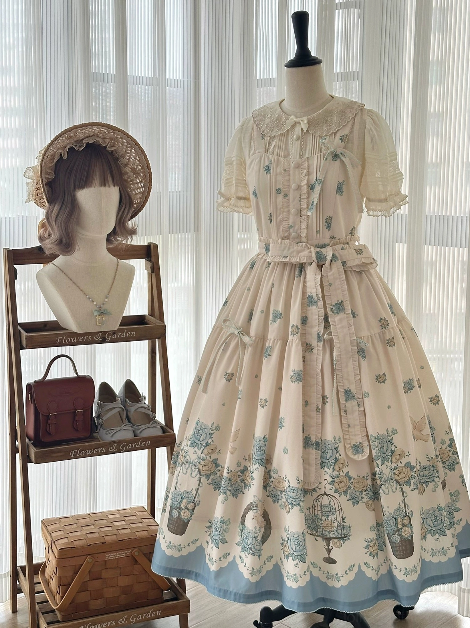 Classic lolita jumper skirt dress form display front view with floral print, blue scalloped hem, ruffled peter pan collar, decorative bow waist sash, straw accessories