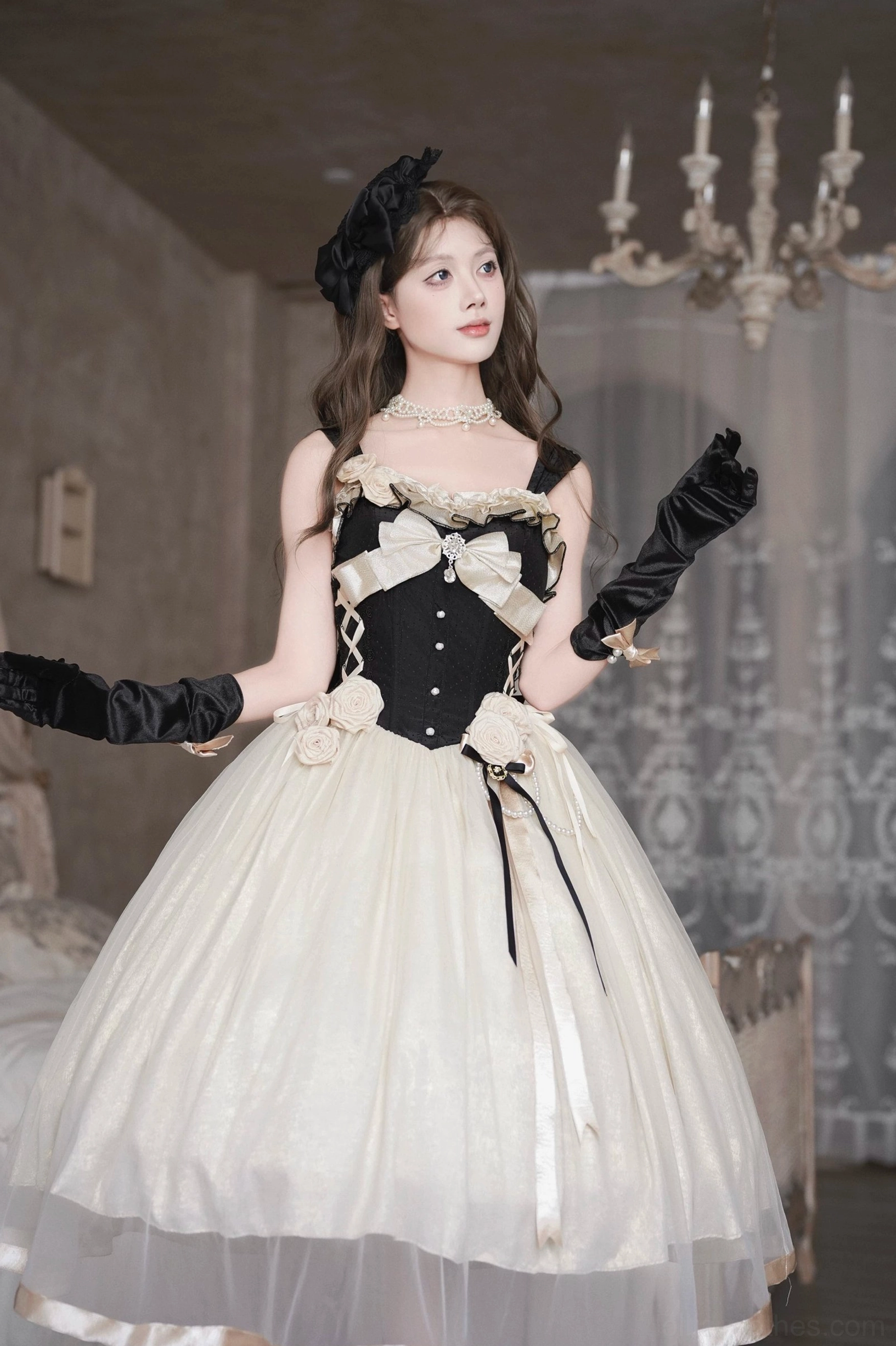Front view of Classic Lolita JSK dress with model posing with raised arms, pearl necklace accessory, structured corset bodice, full flowy tulle midi skirt, chandelier background