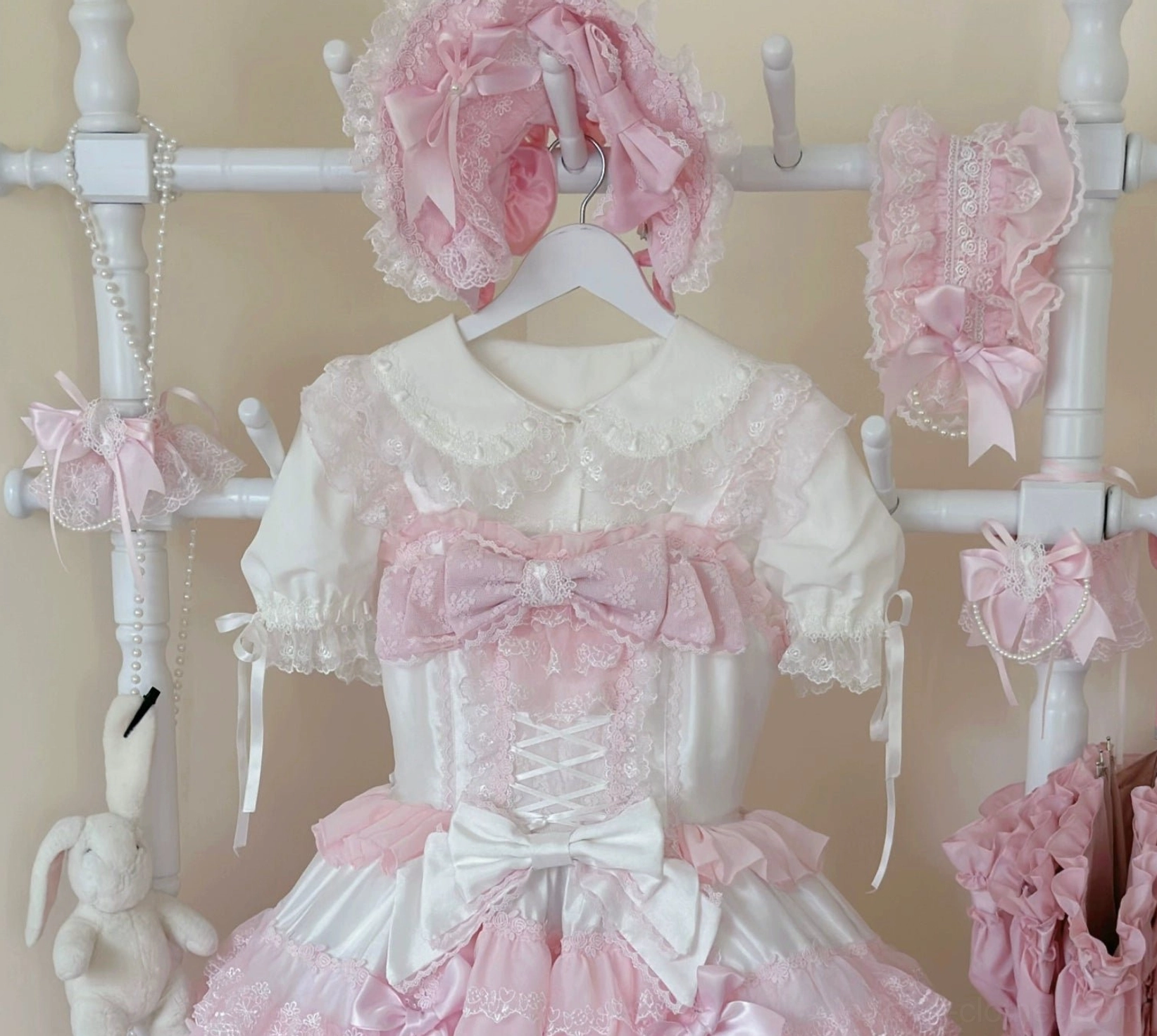 Flat lay display of single lolita outfit set on clothing rack with matching hair ornaments headbow and side clips accessories with stuffed rabbit plush