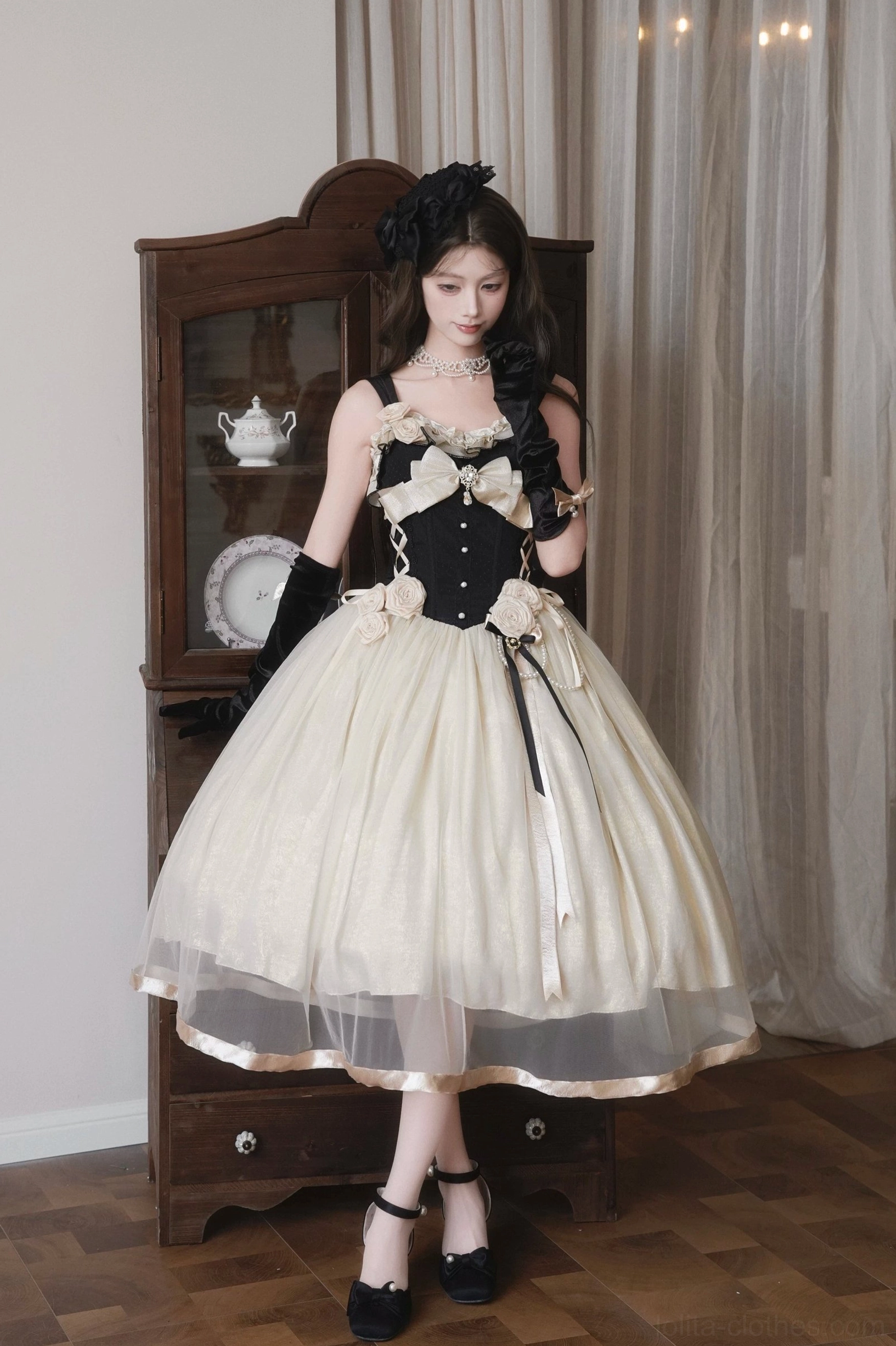 Three-quarter front view of Classic Lolita corset JSK dress with black opera gloves, cream and black color blocking, fitted corset bodice, beside vintage wooden display cabinet