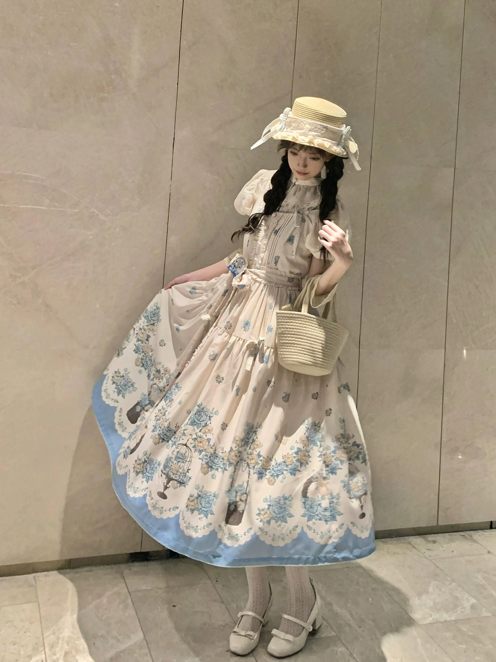 Classic lolita jsk dress full-body side portrait view on model against plain wall, cream with blue floral print, scalloped hem, ruffled neckline, straw boater hat coordination