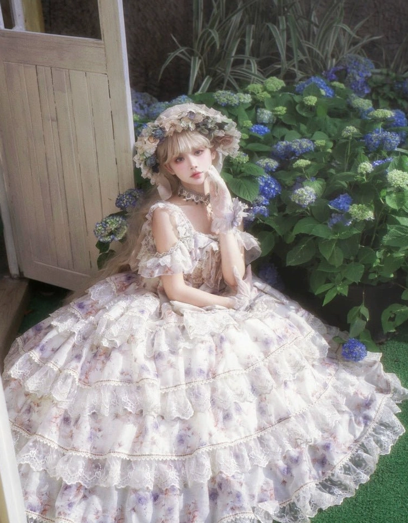 Front side full-body view of purple floral lolita dress featuring off-shoulder ruffled straps, complete ballgown silhouette with lace-trimmed layered skirt, model sitting by hydrangea flowers