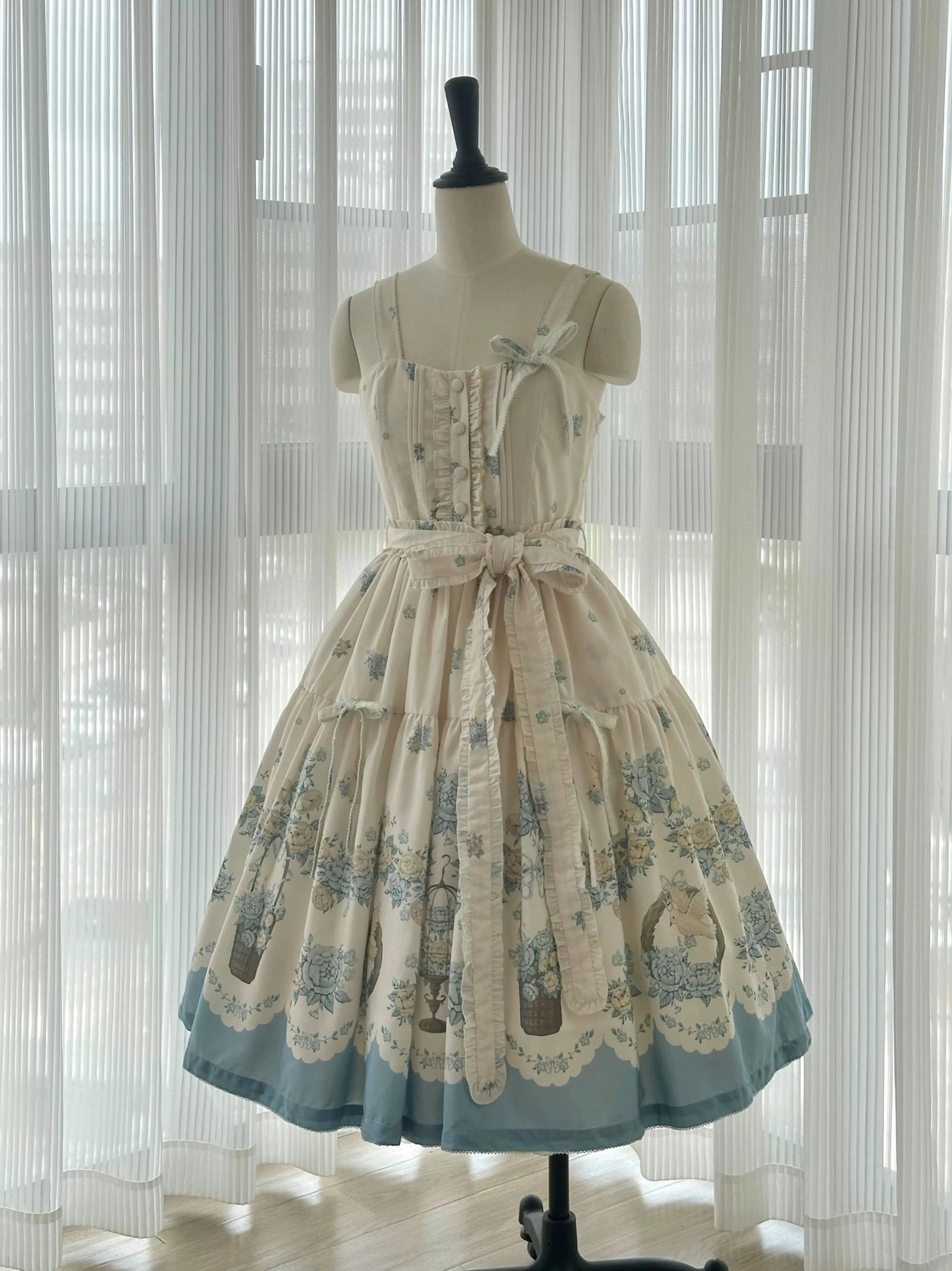 Spaghetti strap classic lolita jumper skirt sleeveless design full-body display, cream fabric with blue floral print, scalloped blue hem, decorative bow sash, button placket