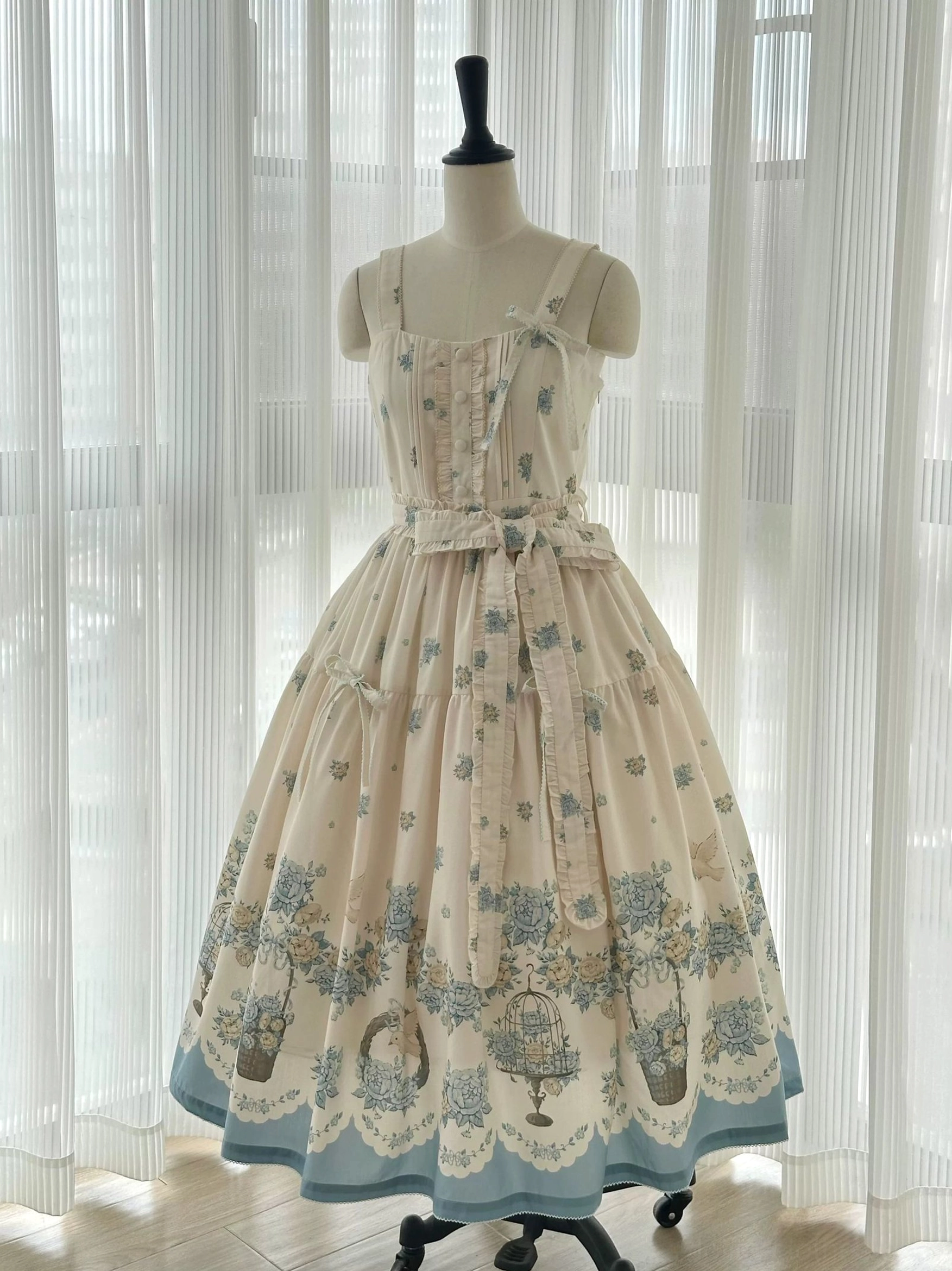 Sleeveless lolita jsk dress three-quarter view on dress form, cream base with blue garden floral botanical patterns, scalloped blue hem, lace front bodice details