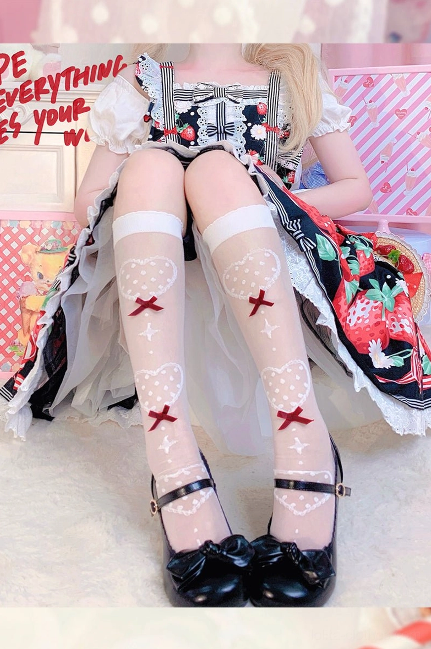 Lower body close-up of Lolita girl in dark patterned dress wearing sheer knee socks with red bow cross heart design and black Mary Jane footwear
