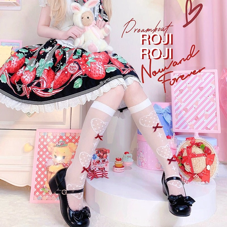 Lower body view of Lolita girl in strawberry print dress wearing sheer nude knee socks with red bow heart patterns paired with black Mary Jane shoes