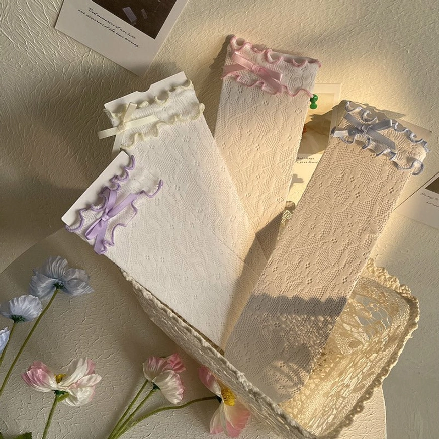 Multiple pairs of Lolita mid-calf lace ankle socks with different colored ribbon bows displayed flat lay on decorative lace tray with small flowers showing color variety