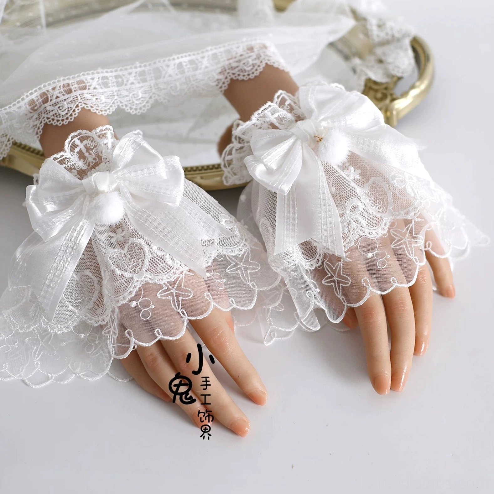 Pair of Lolita lace fingerless cuffs gloves with sheer ruffled edges, satin bows and pom-pom decorations on vintage gold tray