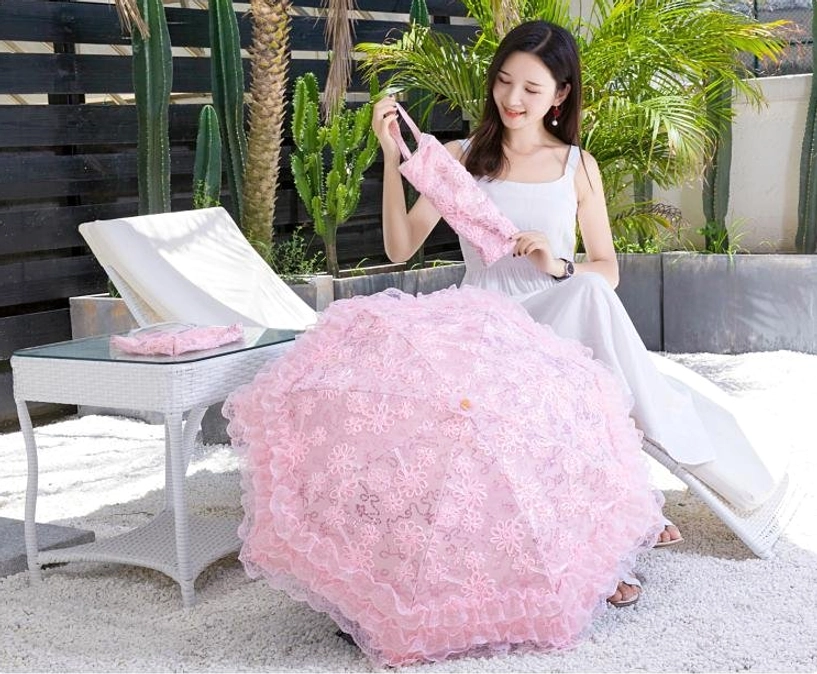 Woman in white long dress relaxing on outdoor lounge chair holding pink lace Lolita parasol, modern garden with rattan furniture and succulent plants background