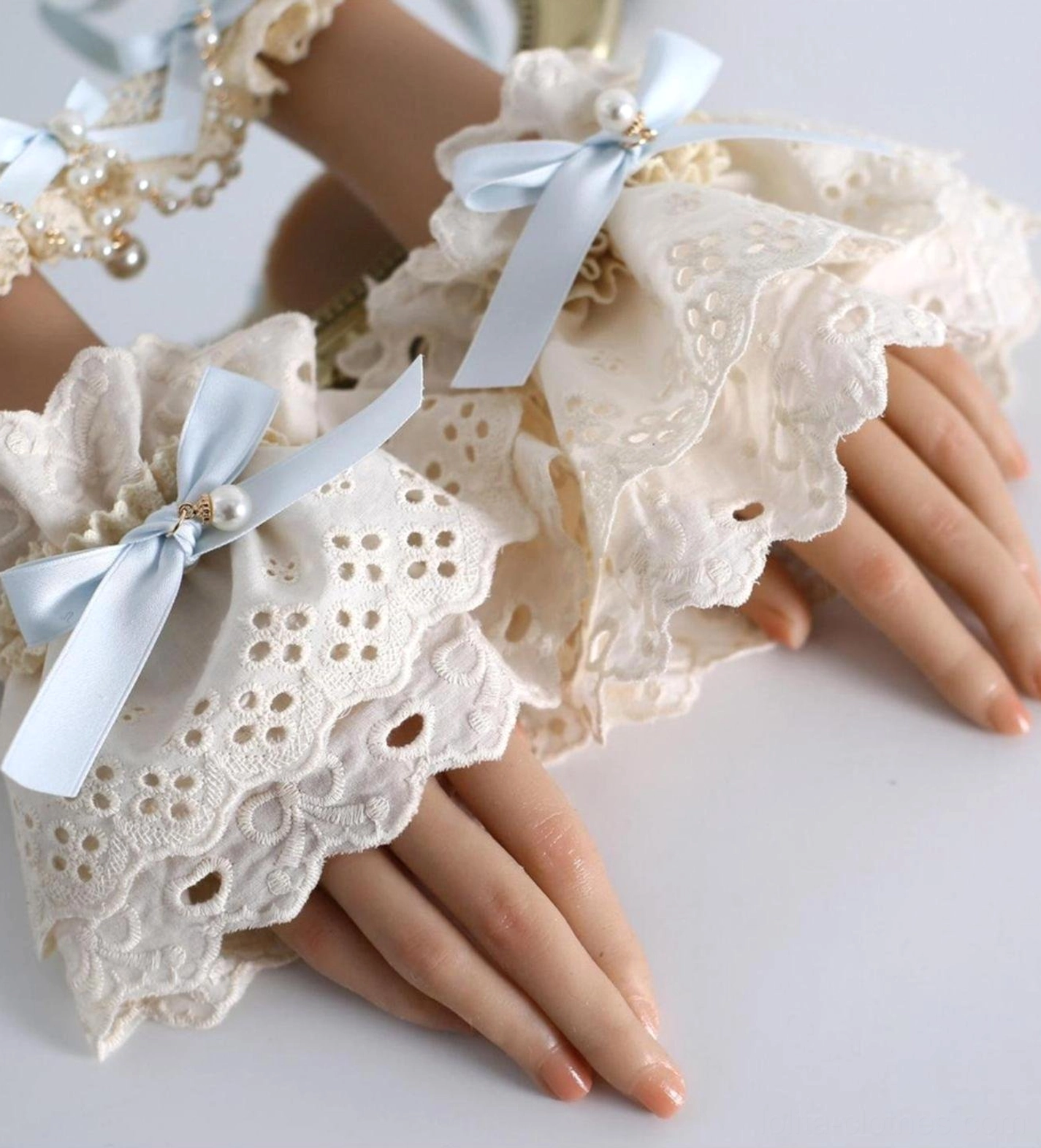Pair of lolita lace wrist cuffs with embroidered eyelet design sky blue bows and pearl details ruffled edges flat lay