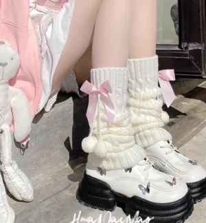White slouchy knit lolita leg warmers with pink detachable bow and fluffy pom-pom trim worn with pink coat and white platform Mary Jane shoes indoor doorway