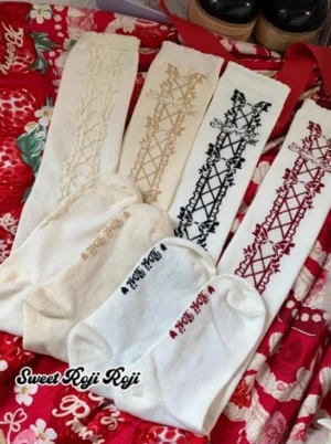 Lolita mid-calf cotton socks with criss-cross bow pattern and decorative embroidery shown in flat lay style on red floral printed fabric, featuring all four color variants