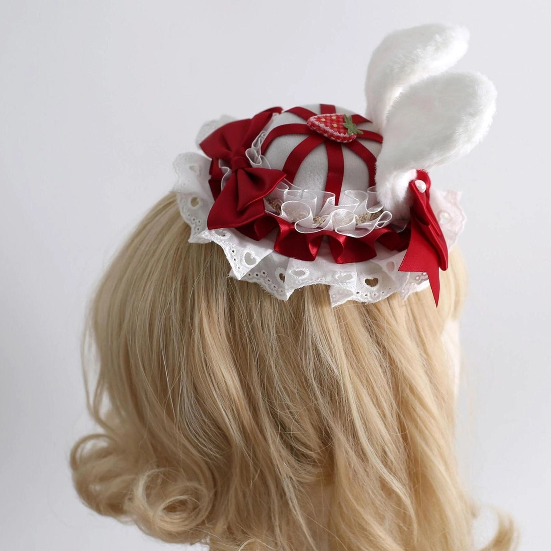 Rear style lolita mini top hat hair accessory featuring fluffy white bunny ears, red striped hat base with strawberry ornament, red bows and white ruffled lace trim back view