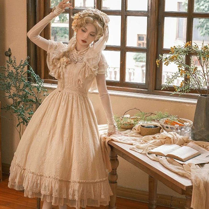 Vintage champagne Lolita OP dress half-body front view with raised arm, model leaning on vintage dining table, ruffled cape sleeves, lace bodice, knee-length ruffled skirt hem, floral hair ornament and pearl necklaces
