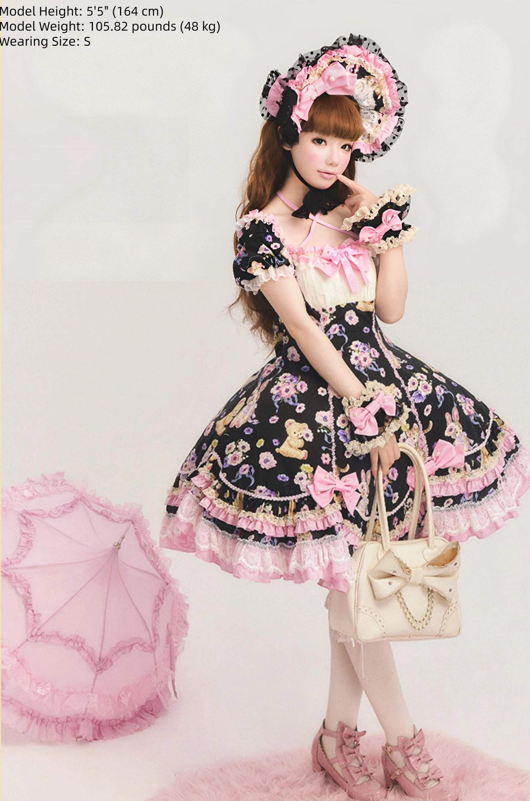 Full-body three-quarter side view of black sweet lolita OP dress with matching lace bonnet and gloves, carrying beige bow-handled handbag, pink lace trims, studio background