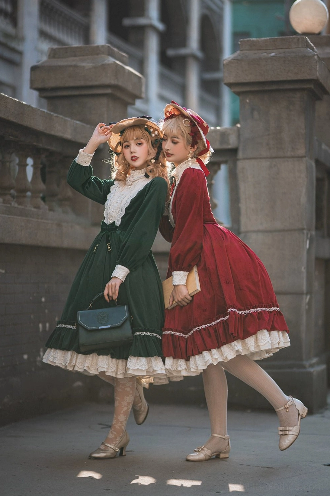 Vintage velvet lolita OP dress front full-body walking shot stone balcony outdoor space two female models dark green dress black handbag red dress golden clutch bag color coordination