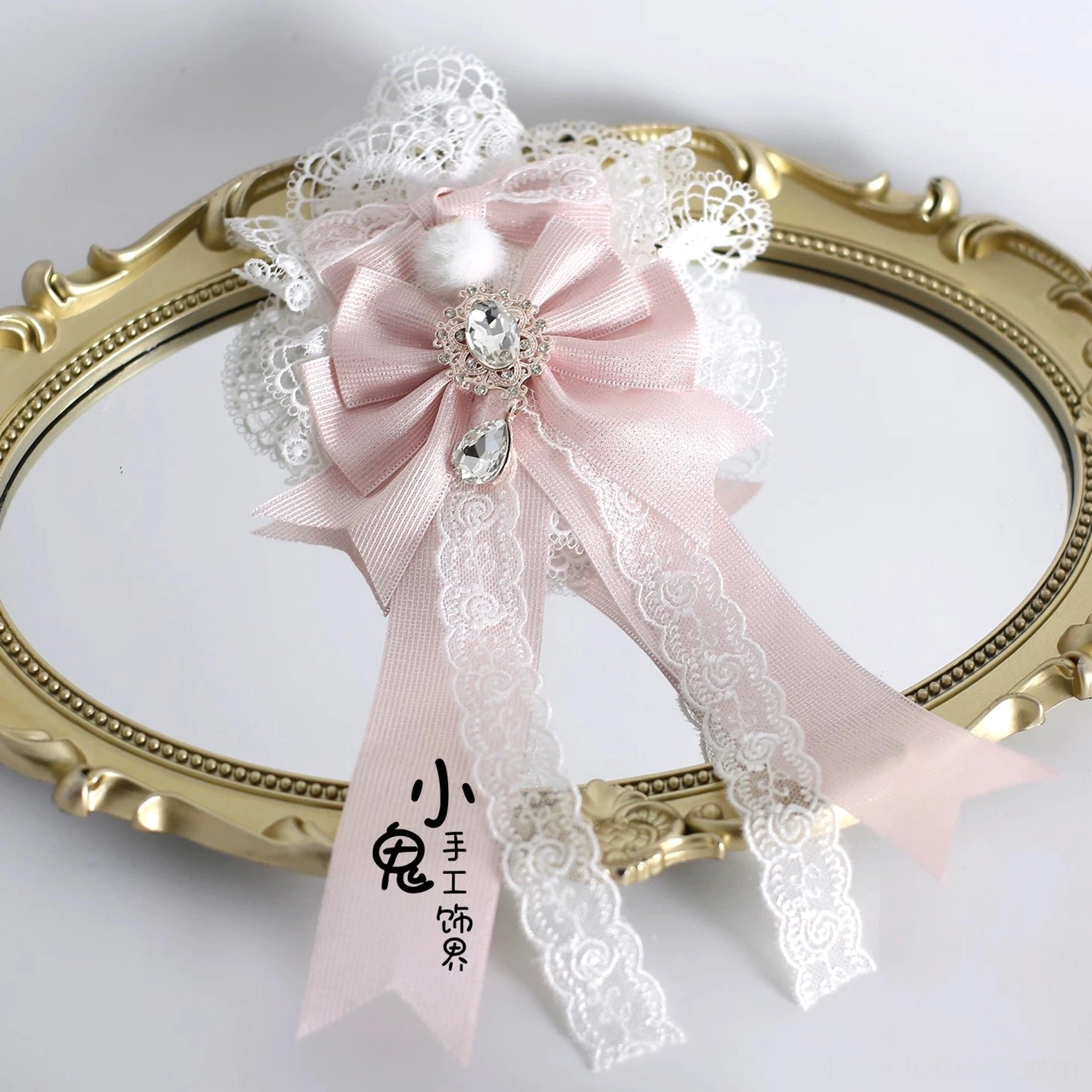Large Lolita oversized bow hair accessory with pink satin construction, heart-shaped rhinestone center detail, long lace tail ribbons, and white lace trim border