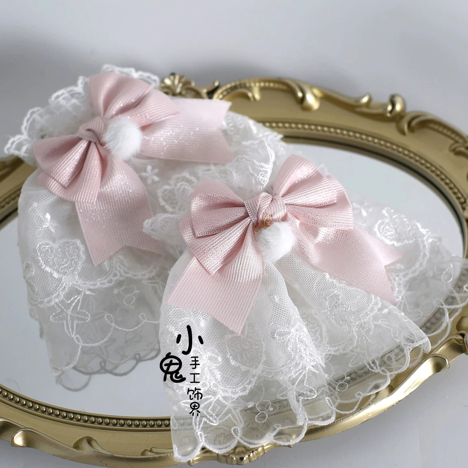 Pair of Lolita lace hair bow clips with white mesh lace base, pink satin bows, fluffy white pom-poms, and soft ruffled trims on vintage mirror