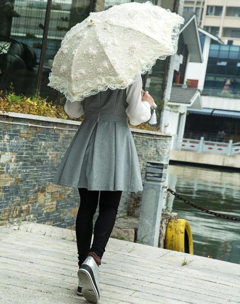 Close-up front view of female model holding open lolita parasol showing black waterproof sun-blocking inner layer, white ruffled lace outer edge, matching tassel pendant on stone terrace