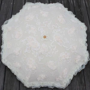 Top-down overhead view of octagonal lace sun parasol on dark wooden surface, showcasing detailed floral lace embroidery, 3D rose appliques, central wooden finial, and scalloped lace border design