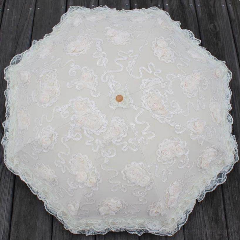 Top-down overhead view of octagonal lace sun parasol on dark wooden surface, showcasing detailed floral lace embroidery, 3D rose appliques, central wooden finial, and scalloped lace border design