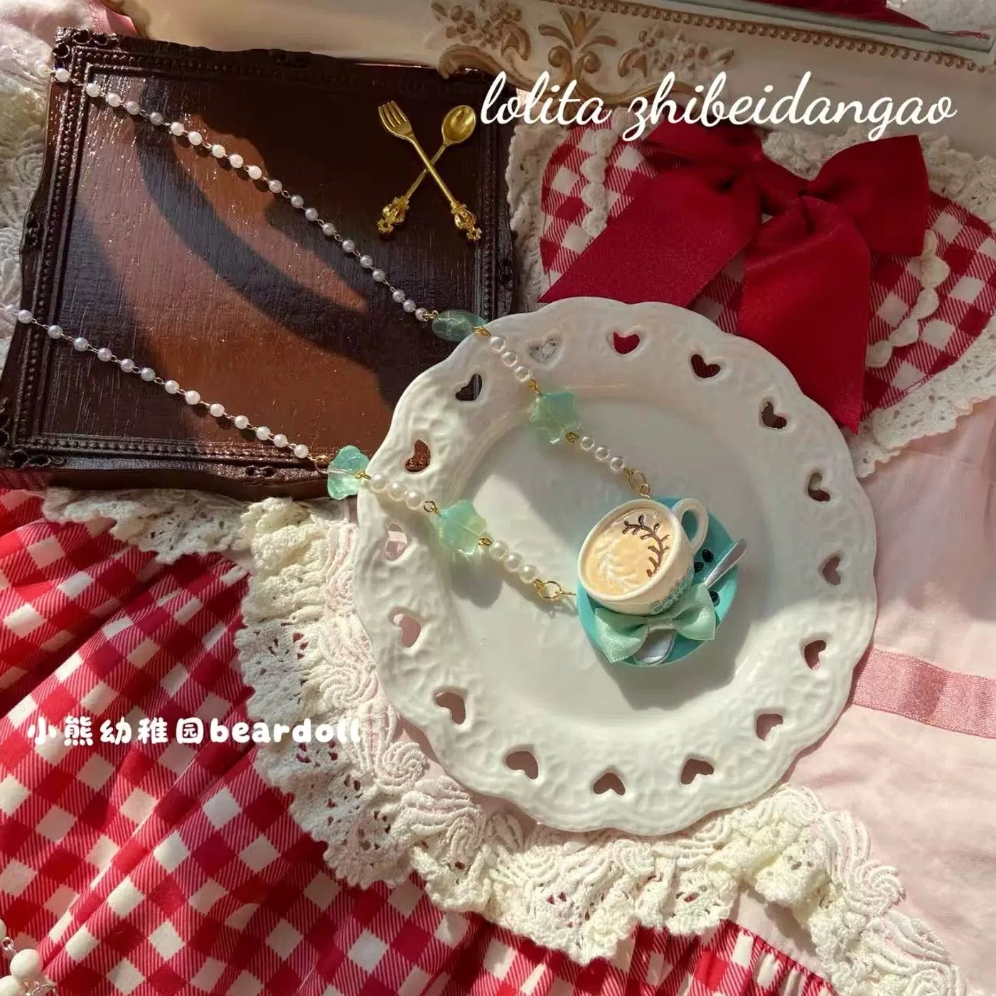 Dainty faux pearl beaded Lolita necklace with small teacup pendant displayed on white heart-shaped ceramic plate surrounded by red gingham fabric and lace doily