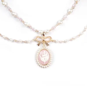Retro bow-accented lolita necklace flat lay showing faux pearl double chain, gold metal bow charm, and pink oval cameo pendant on white background