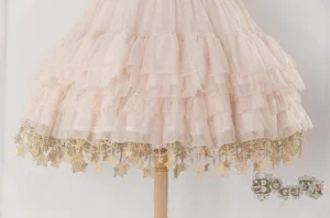 Close-up detail of light beige Lolita underskirt hem showing multi-layered ruffled tulle with delicate gold star hanging tassels