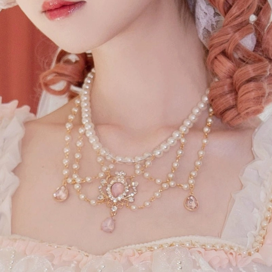 Pink Lolita pearl necklace set with double-layer pearl chains, pink gemstone pendants, and gold rhinestone decorations, worn by model in pink frilly Lolita dress with orange braided hair, close-up neck shot