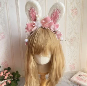 Pink lolita bunny ear headdress worn on blonde mannequin head showcasing large satin bow with pom-pom rabbit decoration and pearl tassel side trims in vintage floral setting